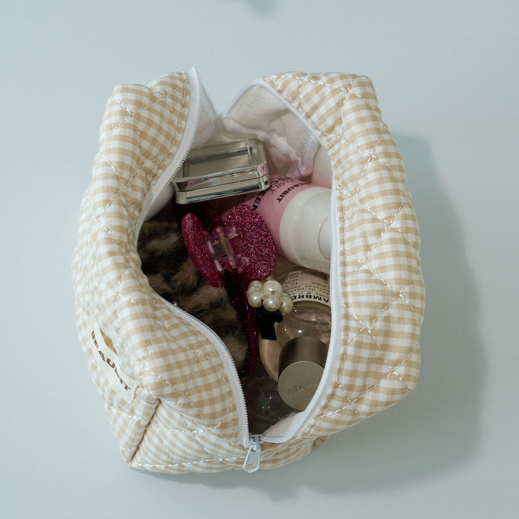 A beige and white checkered cosmetic BEAUBIT pouch filled with various makeup items, shown from a top-down view on a light gray background.
